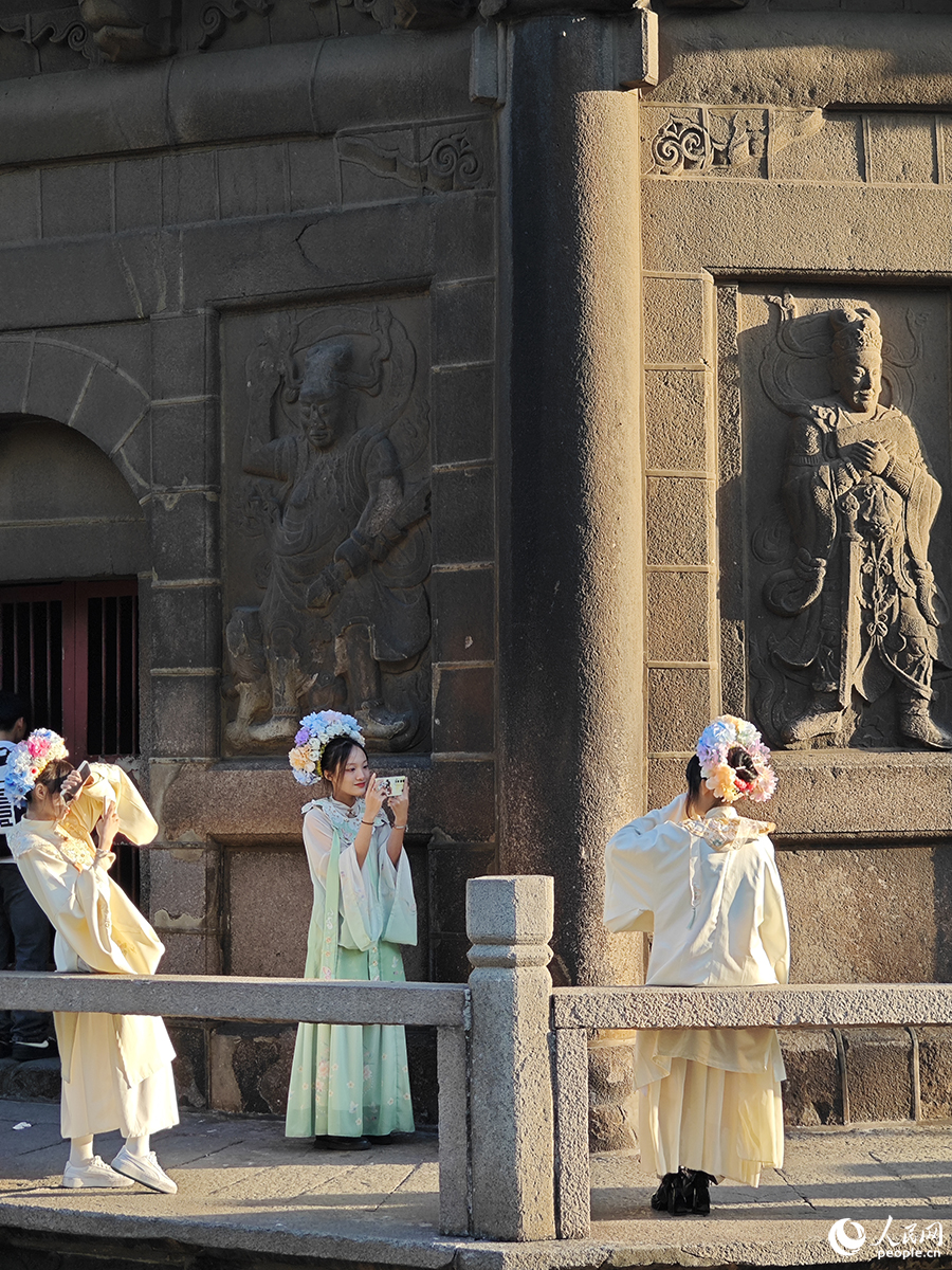 2024年1月18日，三位游客頭戴“簪花”，身著漢服在泉州開(kāi)元寺鎮(zhèn)國(guó)塔下拍照。人民網(wǎng) 黃東儀攝